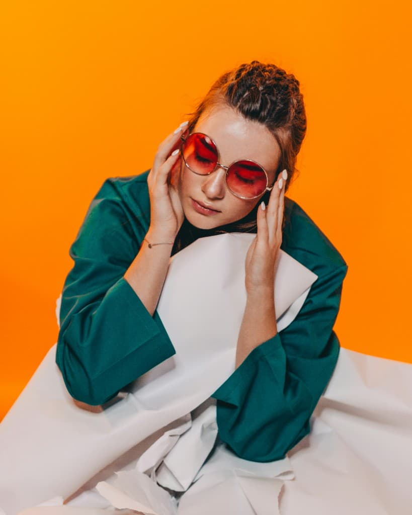 Fashion editorial — red sunglasses and teal blouse against an orange background